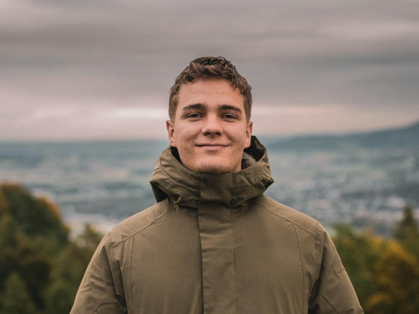 Person wearing a green jacket standing in a field with a scenic background